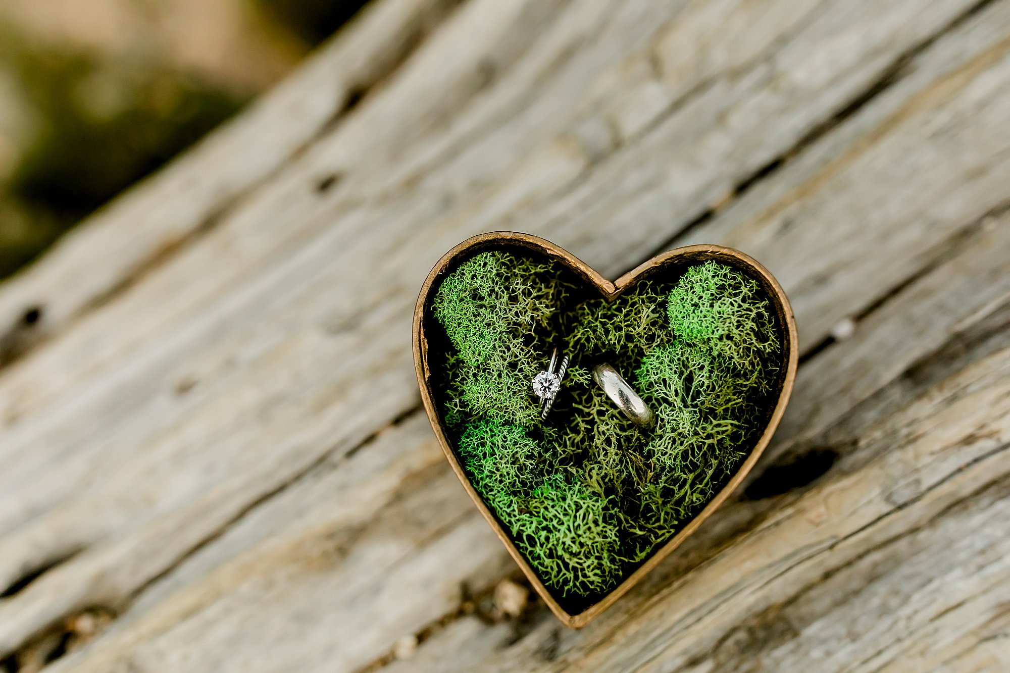 bride and groom rings are placed in a heart shaped box in green moss