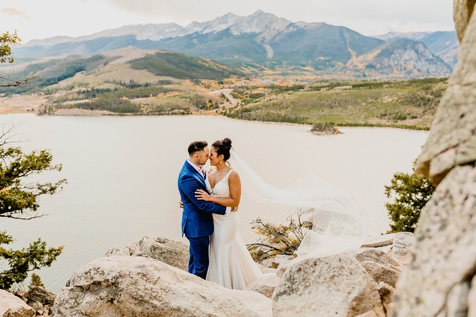 Bride and groom climb on rocks for their Sapphire Point fall elopement with beautiful mountain and lake views behind them