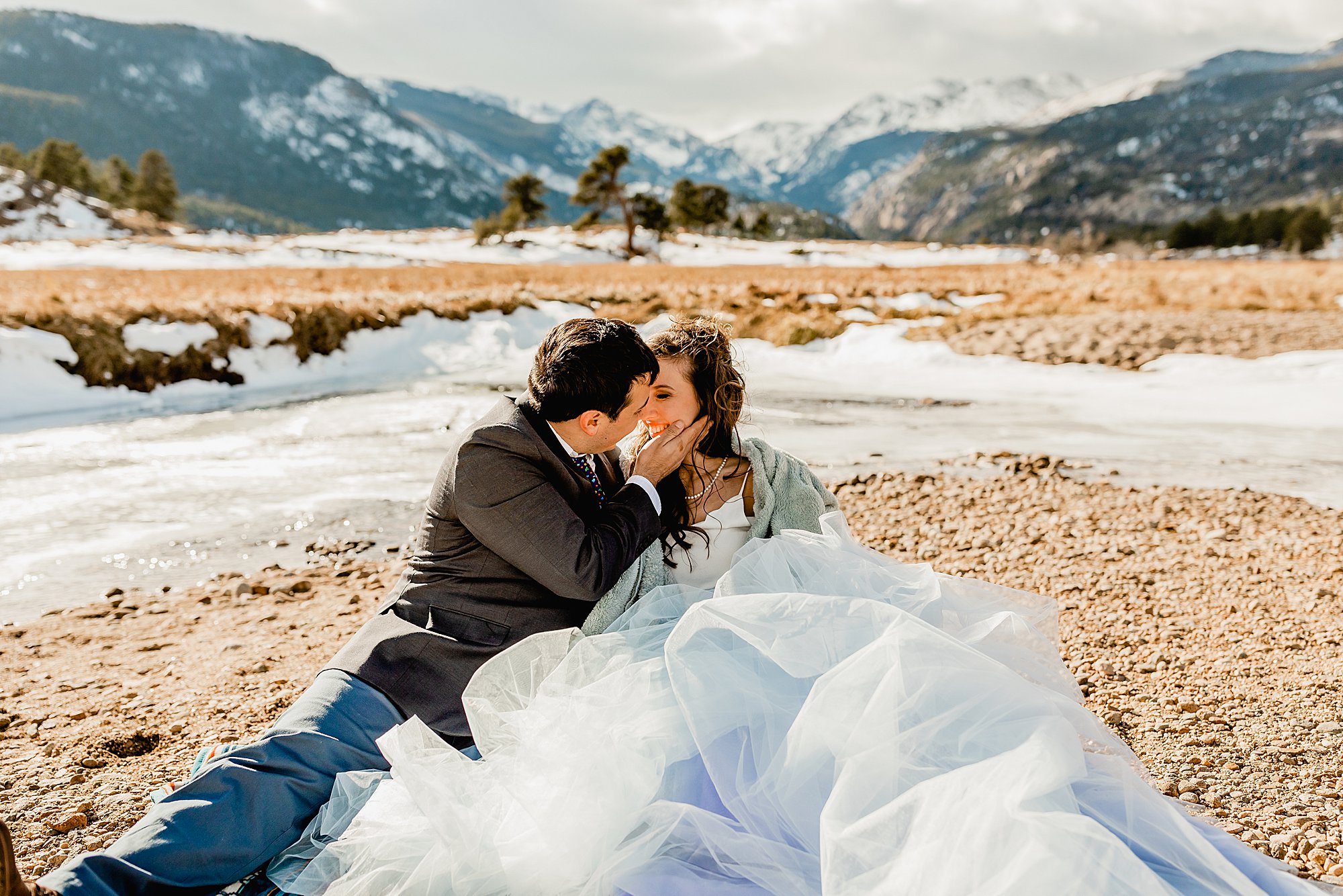 bride and groom cuddle on a blanket for their estes park elopement with beautiful Rocky mountain scenery in the background