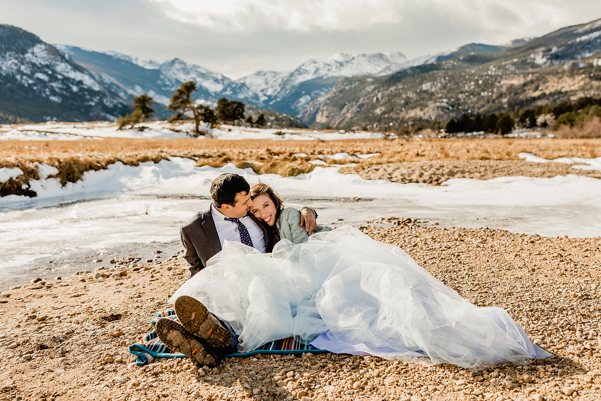 bride and groom cuddle on a blanket for their estes park elopement with beautiful Rocky mountain scenery in the background