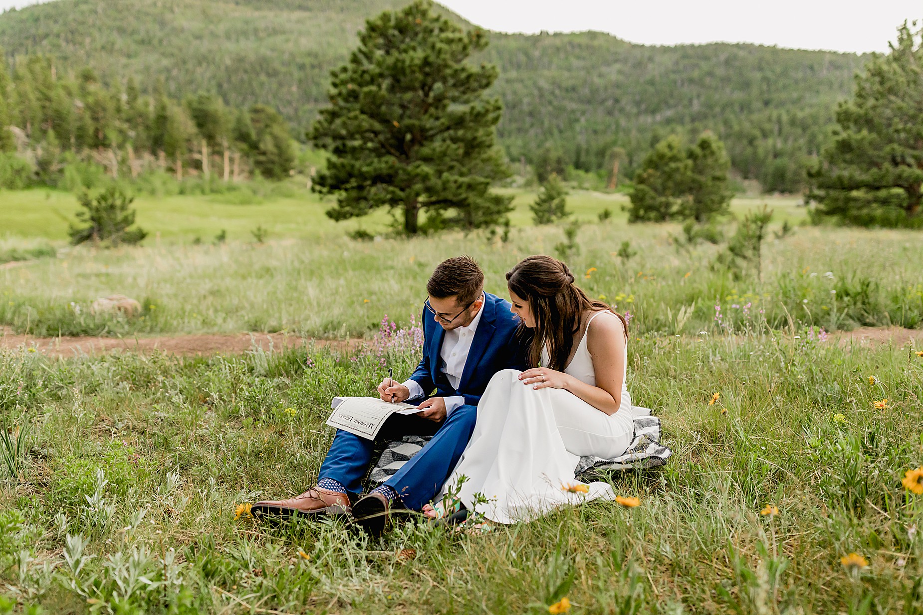 Couple signs marriage license on their Colorado elopement day surrounded by greenery and wildflowers
