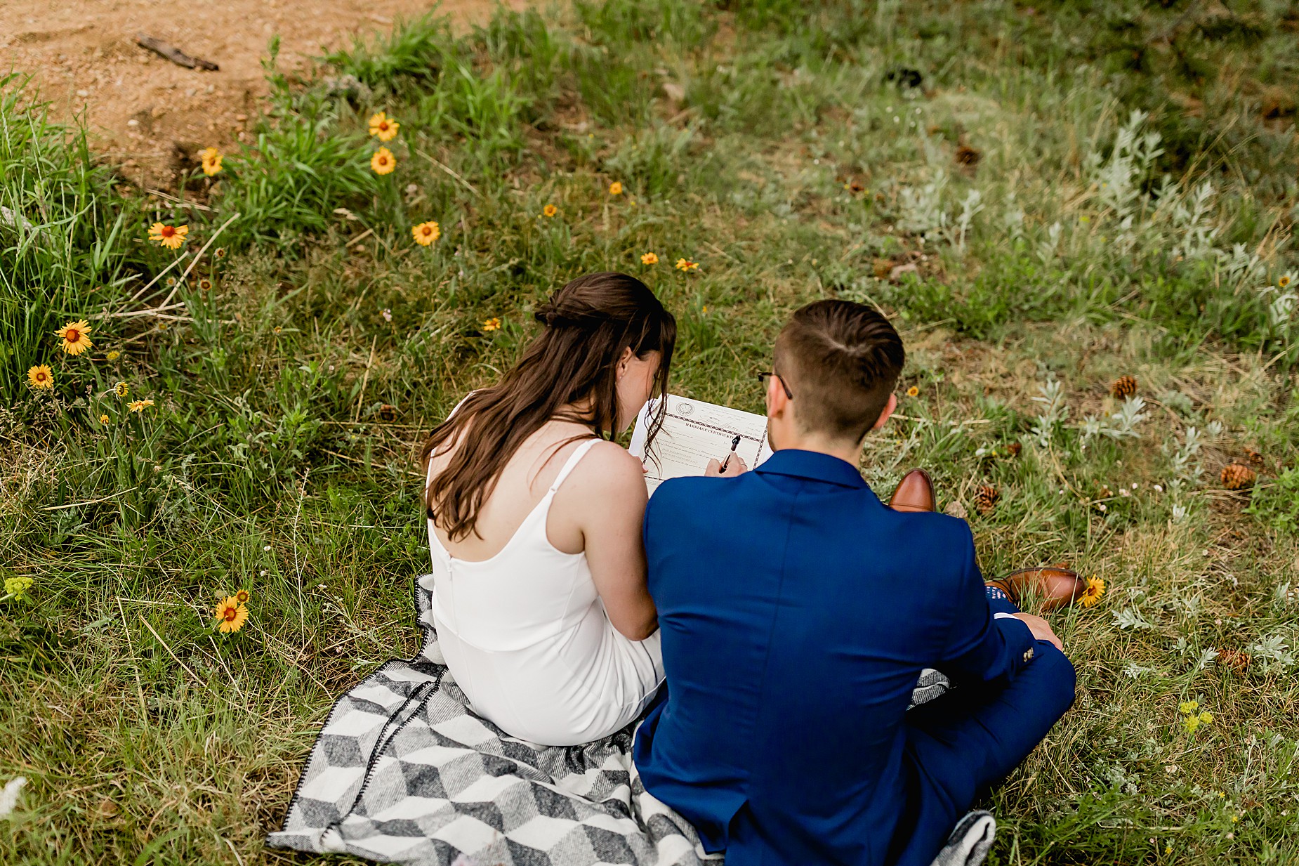 Couple signs marriage license on their Colorado elopement day surrounded by greenery and wildflowers