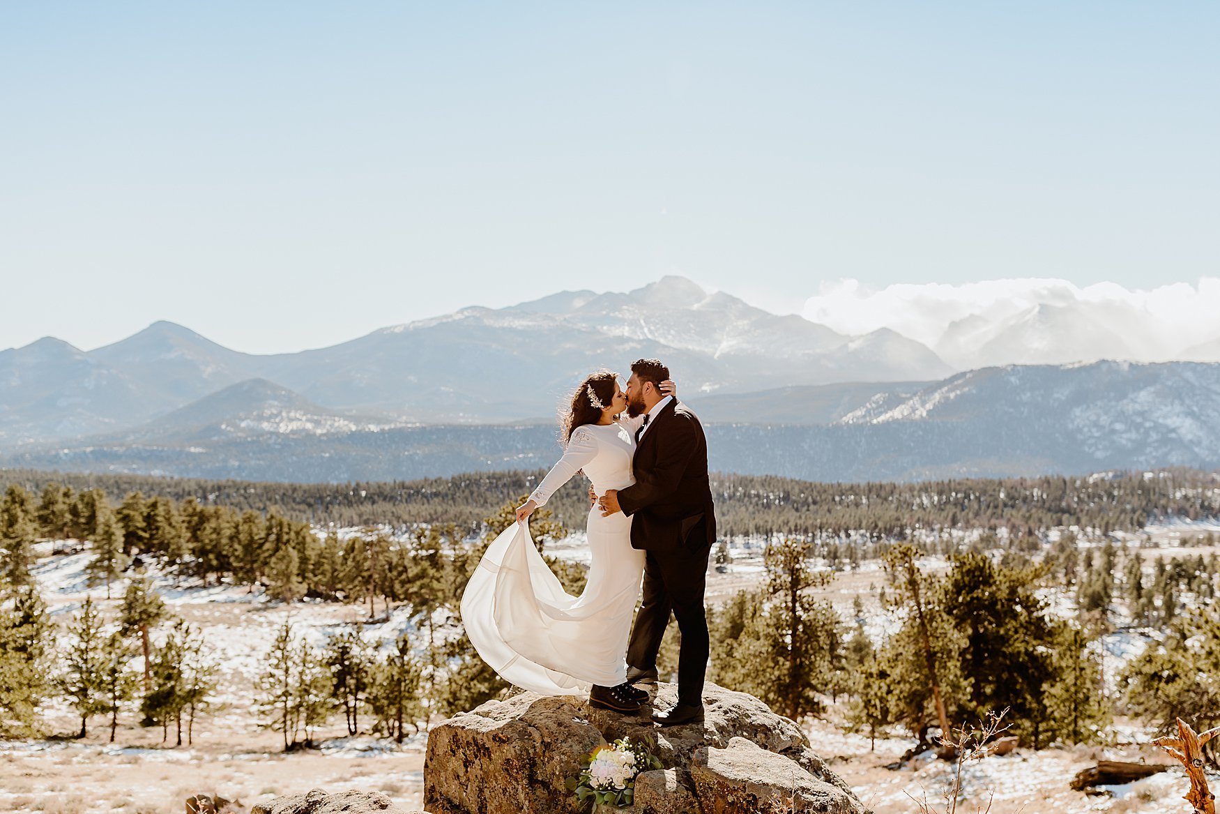 Couple embraces on a rock in front of mountain backdrop in Rocky Mountain National Park for their Colorado winter elopement